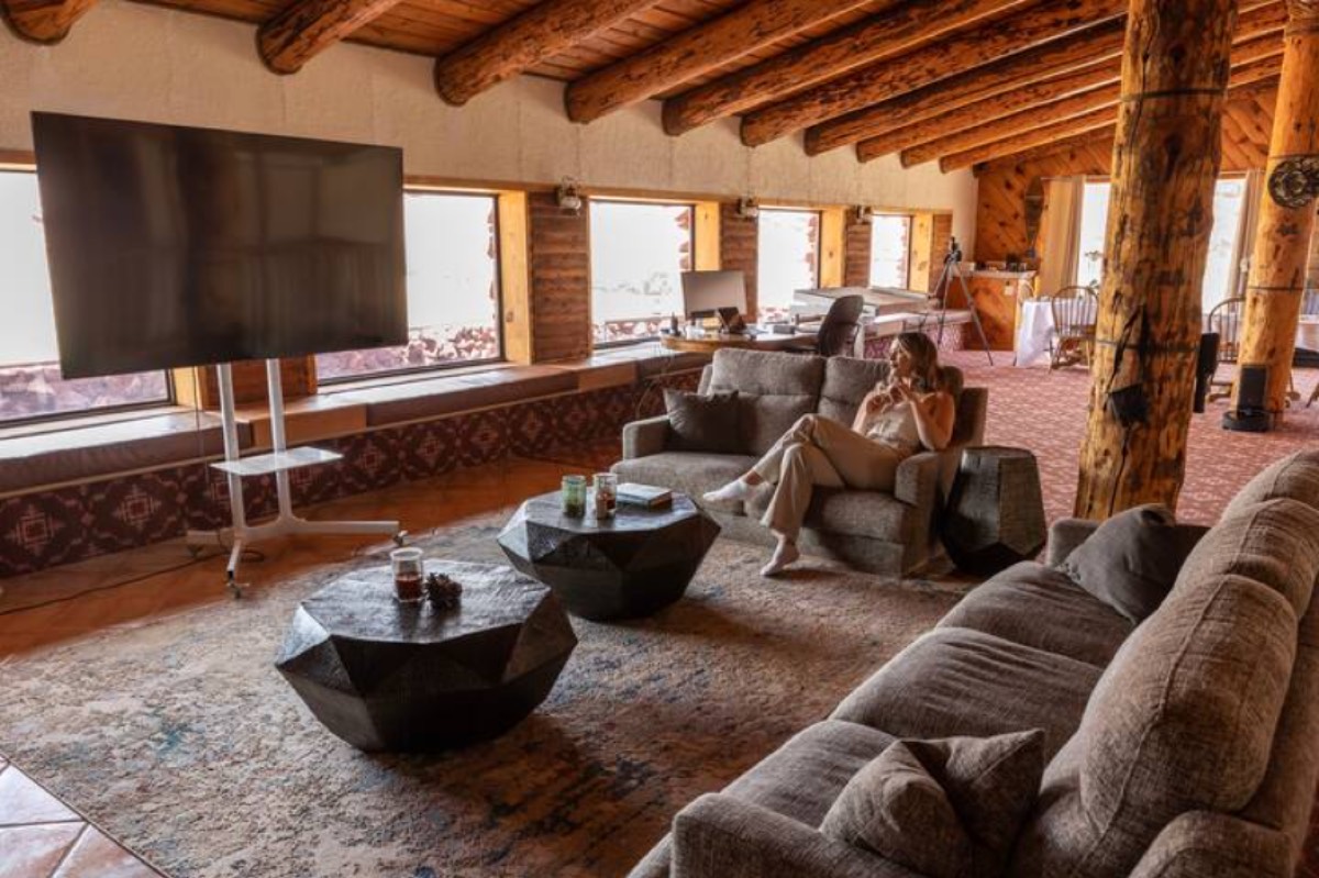 The living room of the Ranch House, log beams above a wall of windows onto the mesa